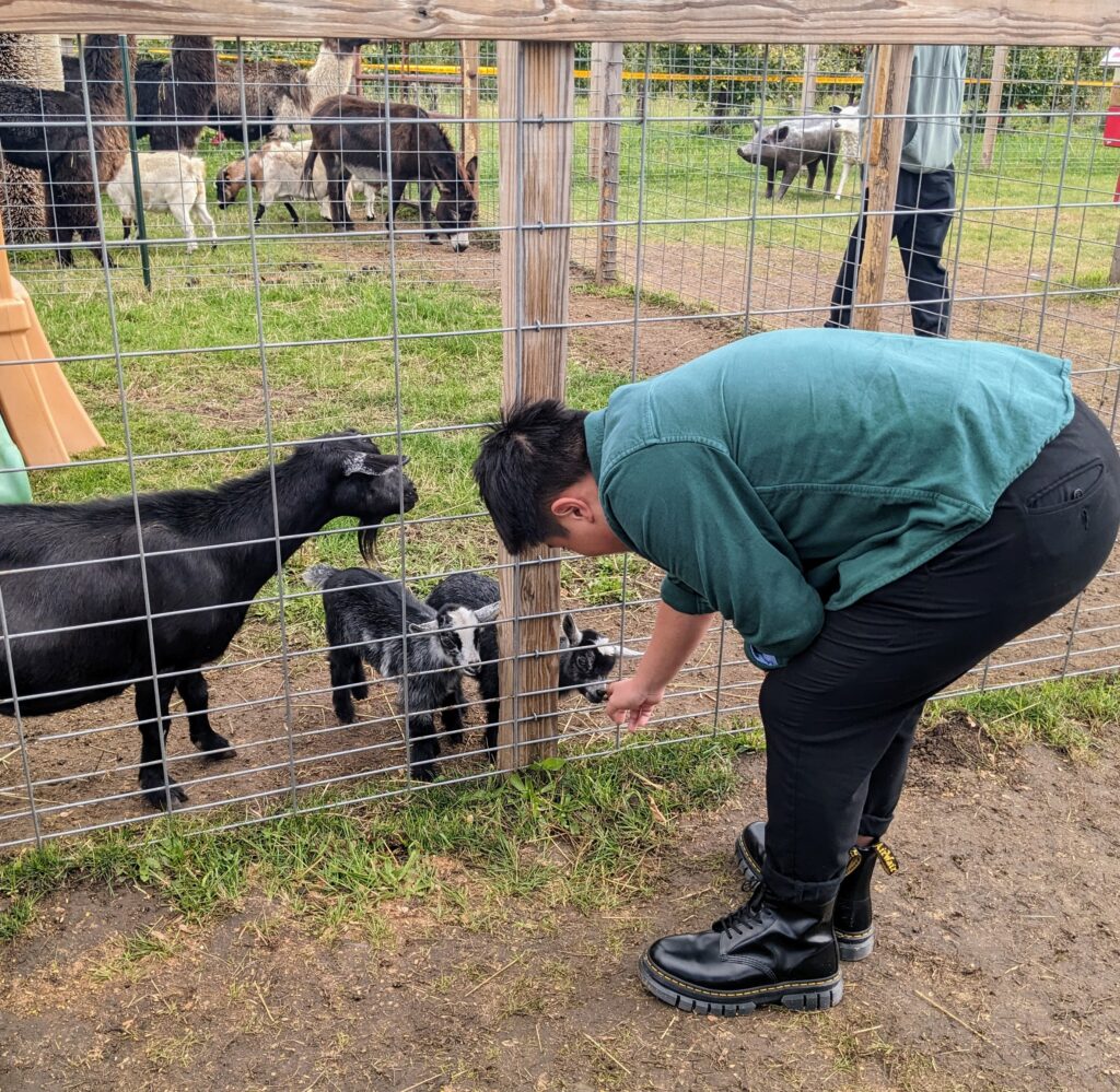 a man bending over to pet a baby goat behind a fence