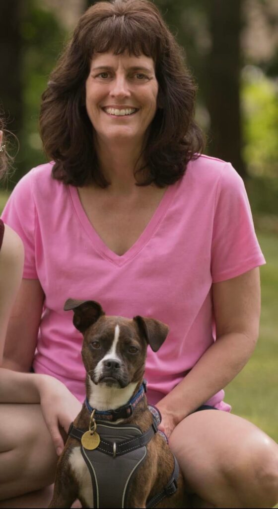 woman smiling with a small brown dog sitting between her legs
